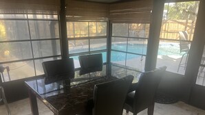 A sunlit room with a glass table and chairs, a view of a backyard with a pool, and a wooden fence. - Private House w/ HEATED Pool and 4 Passes to the Daytona Aquarium & Rainforest! (Port Orange)