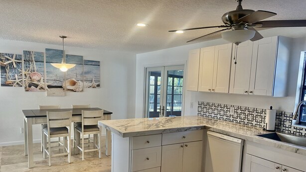 A modern kitchen with white cabinetry, a marble countertop, and a ceiling fan. - Private House w/ HEATED Pool and 4 Passes to the Daytona Aquarium & Rainforest! (Port Orange)