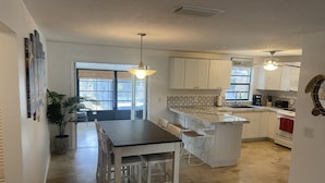 A modern kitchen with white cabinets, a marble countertop, and a dining area with a wooden table and chairs. - Private House w/ HEATED Pool and 4 Passes to the Daytona Aquarium & Rainforest! (Port Orange)