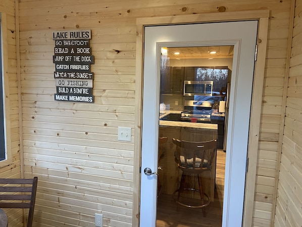 Interno di una baita in legno, con una zona cucina visibile attraverso una porta di vetro.
