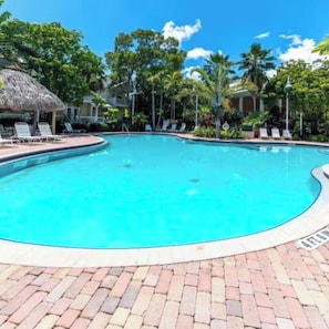 A swimming pool with lounge chairs and a thatched-roof structure. - Beautiful Key West Cottage (Key West)