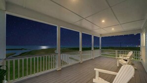 Une terrasse extérieure couverte, dotée de rampes blanches, d’un plancher en bois et de fauteuils Adirondack.