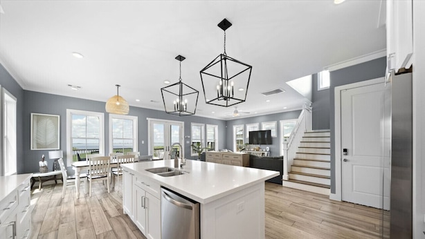 Une cuisine moderne dotée d’un grand îlot central, de meubles blancs et d’un évier intégré à l’îlot. Des luminaires suspendus sont placés au-dessus de l’îlot, et un escalier mène à un autre niveau.