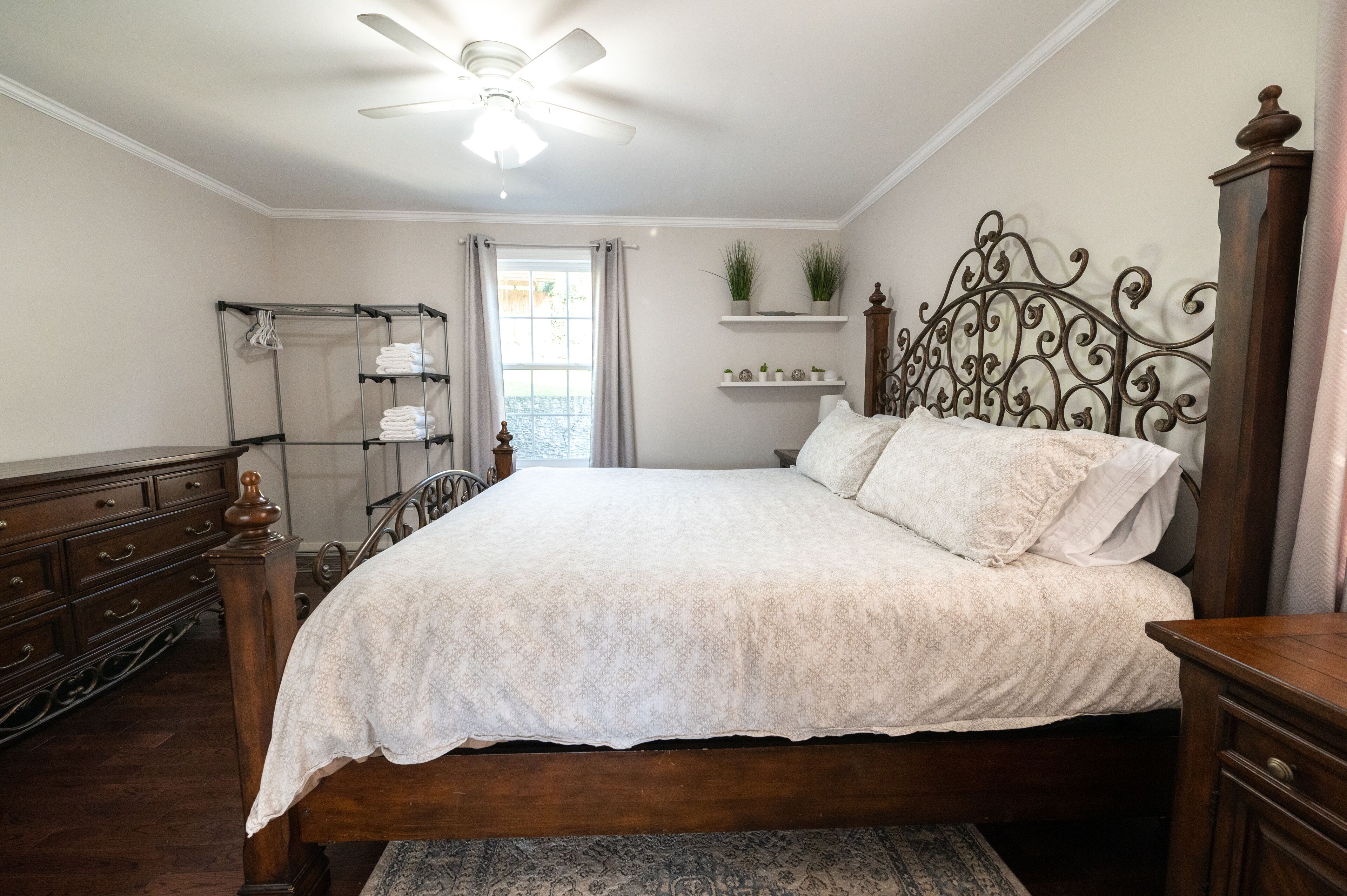 A bedroom with a wooden bed, a ceiling fan, a window with curtains, and a wooden dresser.