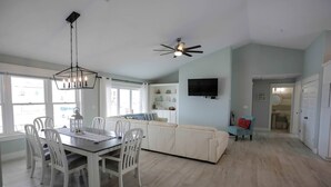A spacious living area with a dining table, white chairs, a sofa, and a TV mounted on the wall. - OHana, Picturesque Home for Tranquil Travels (Navarre)