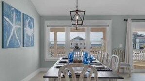 A dining area with a large table, chairs, and a view of the ocean through large windows. - OHana, Picturesque Home for Tranquil Travels (Navarre)