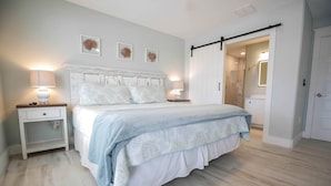A bedroom with a bed, bedside tables, and a door leading to a bathroom. - OHana, Picturesque Home for Tranquil Travels (Navarre)