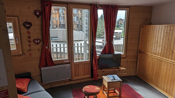 A cozy room with a wooden interior, a sofa, a small table, and a TV. - Avoriaz - charming studio with balcony in the heart of the resort (Morzine)