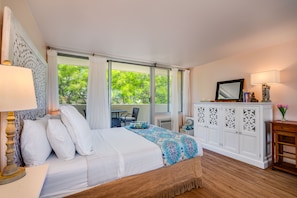Relax in a serene bedroom with a large bed, wooden floor, and a beautiful view of lush greenery.