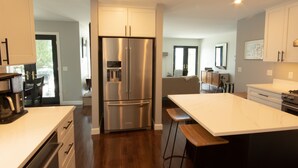 A modern kitchen with stainless steel appliances, a large island, and a dining area. - Sunsets, Sandy Beach and Seclusion; enjoy them all at this stunning lake house (Beaver Island)