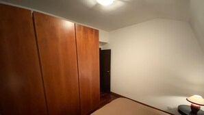 Een slaapkamer met een grote kast, een nachtkastje met een lamp, en een deur naar een andere kamer.