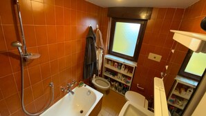 Een badkamer met een badkuip, toilet en planken met toiletartikelen.