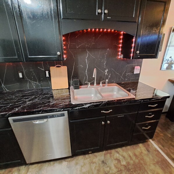 A kitchen with dark cabinets, a marble countertop, a double sink, and a dishwasher.