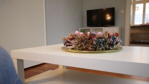 A white table with a floral arrangement in a room with a television and a window. - Vacation apartment Altes Pfarrhaus Bargen 2 persons (Helmstadt-Bargen)