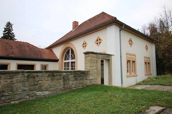 Ein zweistöckiges Gebäude mit einer Steinwand, einem roten Ziegeldach und einer kleinen Grünfläche.