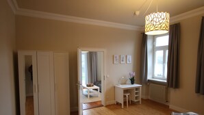 A room with a wooden floor, a white desk, a chair, a bed with plaid bedding, a wardrobe, and a window with curtains. - Vacation apartment Altes Pfarrhaus Bargen 2 persons (Helmstadt-Bargen)