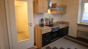 A compact kitchen with wooden cabinets, a built-in oven, and a window with a view. - Vacation apartment Altes Pfarrhaus Bargen 2 persons (Helmstadt-Bargen)