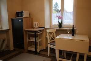 Eine kleine Küche mit Mikrowelle, Wasserkocher und einem Tisch mit einer Weinflasche und Gläsern.