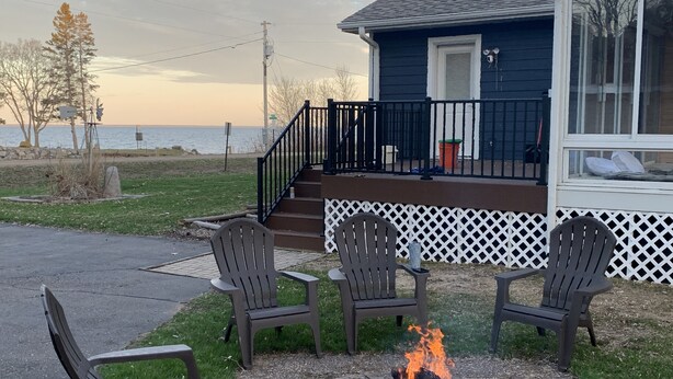A house with a deck, three Adirondack chairs, and a fire pit. - Mille Lacs Lake Cabin, perfect, convenient  location for all outdoor activities! (Aitkin)
