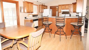 A kitchen with wooden cabinets, a central island with bar stools, a dining table with chairs, and a refrigerator. - Mille Lacs Lake Cabin, perfect, convenient  location for all outdoor activities! (Aitkin)