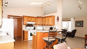 A kitchen with wooden cabinets, a white refrigerator, a stove, and a dining area with a table and chairs. - Mille Lacs Lake Cabin, perfect, convenient  location for all outdoor activities! (Aitkin)