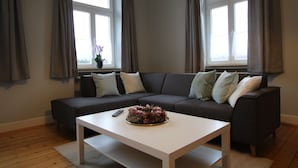 Ein modernes Wohnzimmer mit einem dunkelgrauen Sofa, einem weißen Couchtisch und einer Fernbedienung auf dem Tisch.