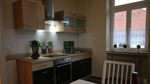 Eine Küche mit Holzschränken, einem Geschirrspüler, einem Fenster mit Spitzenvorhängen und Topfpflanzen.