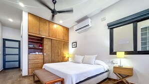 A bedroom with a bed, bedside tables, a bench, a wardrobe, and an air conditioning unit. - Steps From Ocean with Pool! (Isla Mujeres)