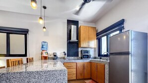 A modern kitchen with granite countertops, wooden cabinets, a stainless steel refrigerator, and a built-in oven. - Steps From Ocean with Pool! (Isla Mujeres)