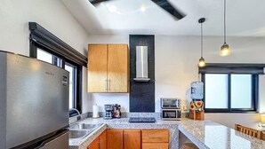 Eine moderne Küche mit Granit-Arbeitsplatten, Holzschränken, einem Edelstahl-Kühlschrank, einem Einbauofen und einem Wasserspender.