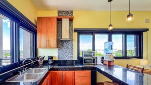 Een moderne keuken met houten kastjes, een zwart aanrecht en een stadsgezicht door grote ramen.