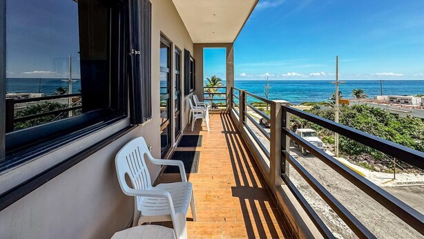 Een balkon met uitzicht op zee, witte plastic stoelen en een houten vloer.