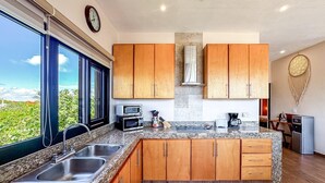 A modern kitchen with granite countertops, wooden cabinets, a built-in oven, and a large window offering a view of greenery. - Ocean View 6 BR House Steps from Ocean! (Isla Mujeres)