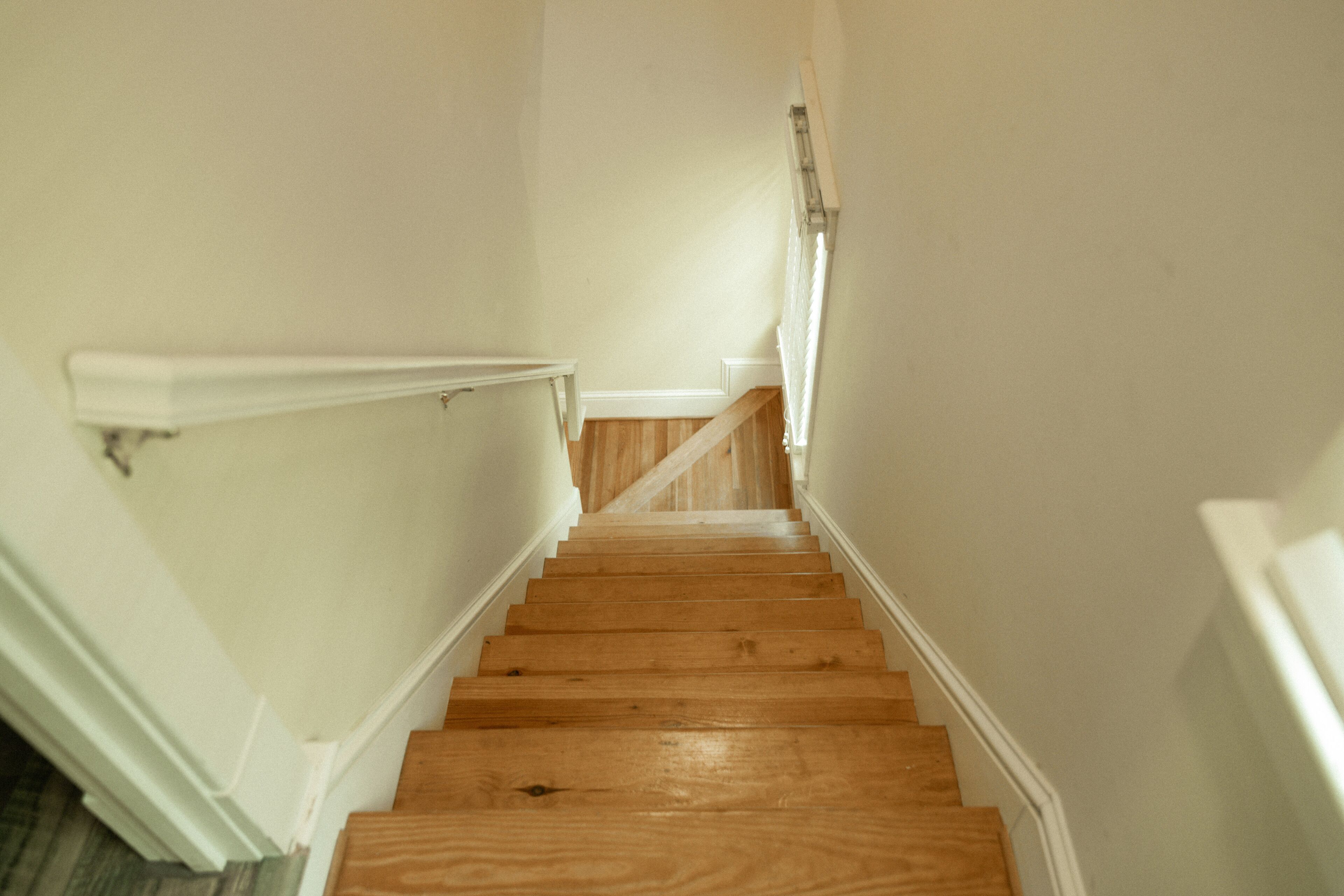 Un escalier en bois, avec des murs blancs et une rampe blanche.