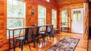 A wooden cabin interior with a dining area, large windows, and a door. - Riverfront • Hot Tub • Convenient Location (Blue Ridge)