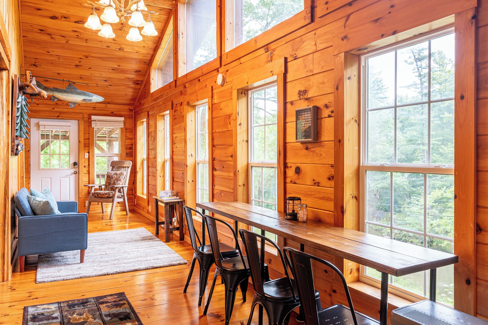 Une cabane avec une longue table à manger, plusieurs chaises, un canapé et une cheminée.