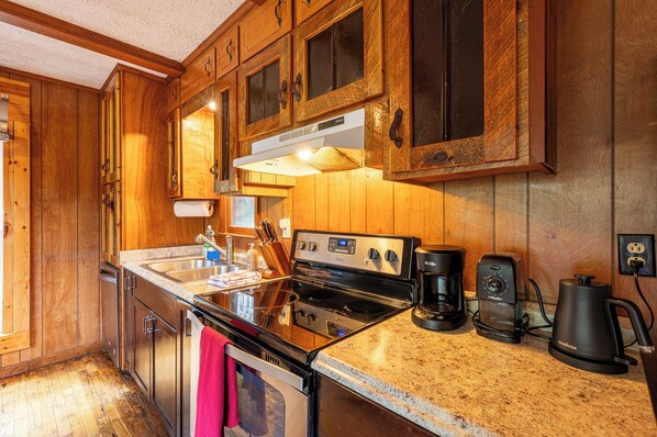 A kitchen with wooden cabinets, a stainless steel sink, a stove, and a coffee maker.