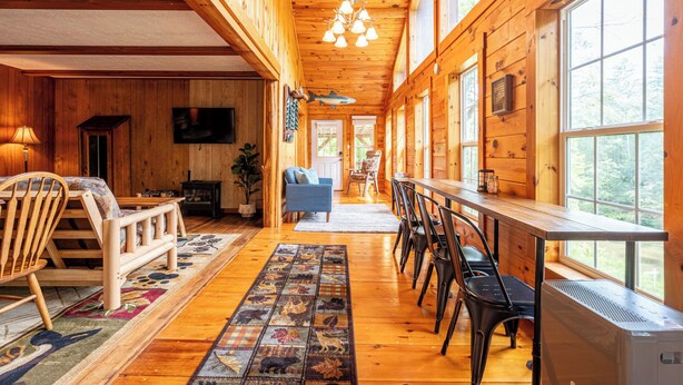 A wooden cabin interior with a dining area, a TV, and a fireplace. - Riverfront • Hot Tub • Convenient Location (Blue Ridge)