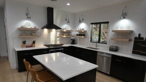 A modern kitchen with a central island, black cabinets, white countertops, and pendant lighting.