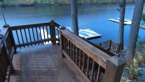 A wooden deck with a railing overlooking a lake, surrounded by trees.