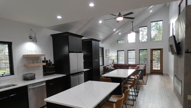 A modern kitchen with a central island, black cabinets, and a dining area with a long table and chairs.