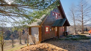 Une cabane en rondins avec un toit à forte pente, un porche à l’avant et une petite terrasse.