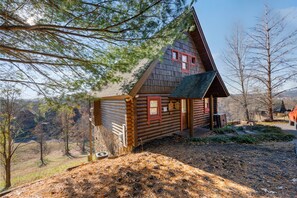 Une cabane en rondins avec un toit à forte pente, un porche à l’avant et une petite terrasse.