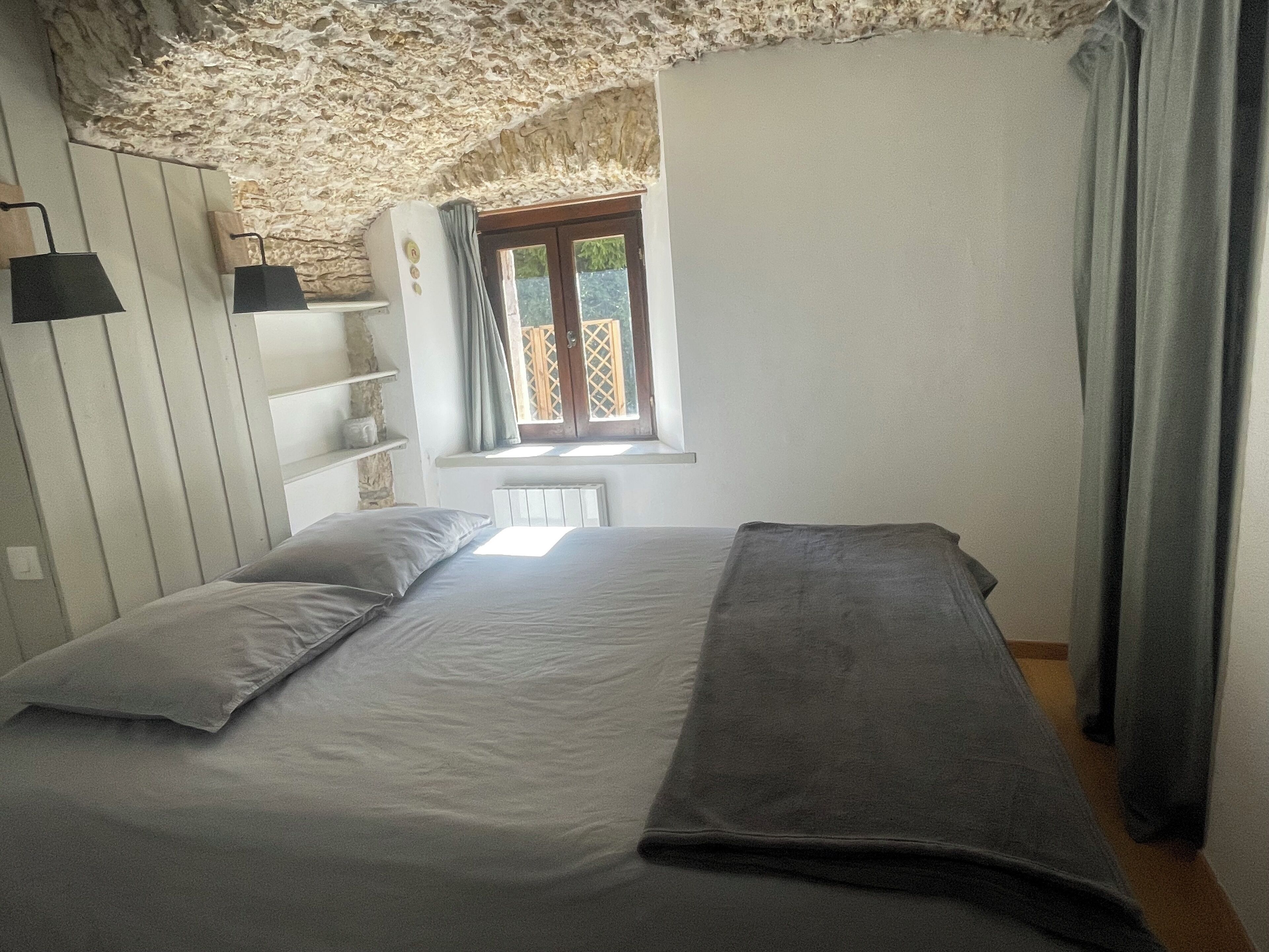 Ein Schlafzimmer mit einem Bett, zwei Nachttischen, einem Fenster mit Vorhängen und einer Steinsäule.
