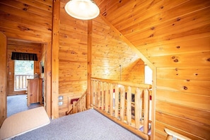 A wooden cabin interior with a staircase, a small desk, and a view of the outdoors.