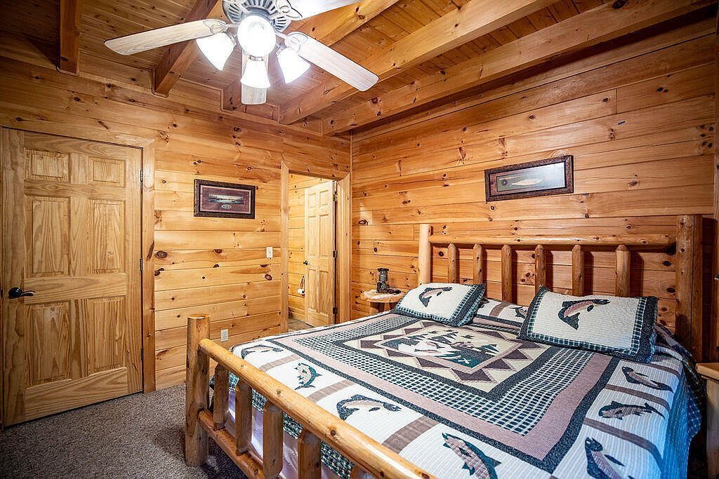 Une chambre dans une cabane en bois, avec un lit, un ventilateur de plafond et deux tableaux encadrés accrochés au mur.