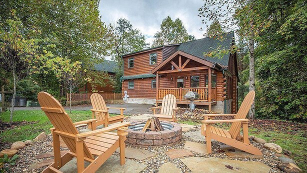 Eine Holzhütte mit Feuerstelle und Adirondack-Stühlen im Garten.