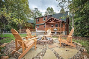 A log cabin with a fire pit and Adirondack chairs in the yard.