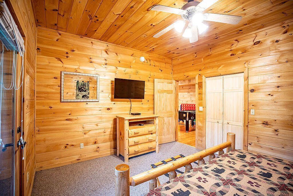 Habitació d'una cabana de fusta amb un ventilador de sostre, televisió penjada, una banca de fusta i una catifa estampada.