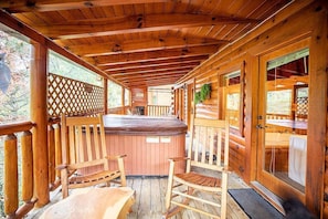 A wooden deck with a hot tub, wooden chairs, and a glass door leading to a bathroom.